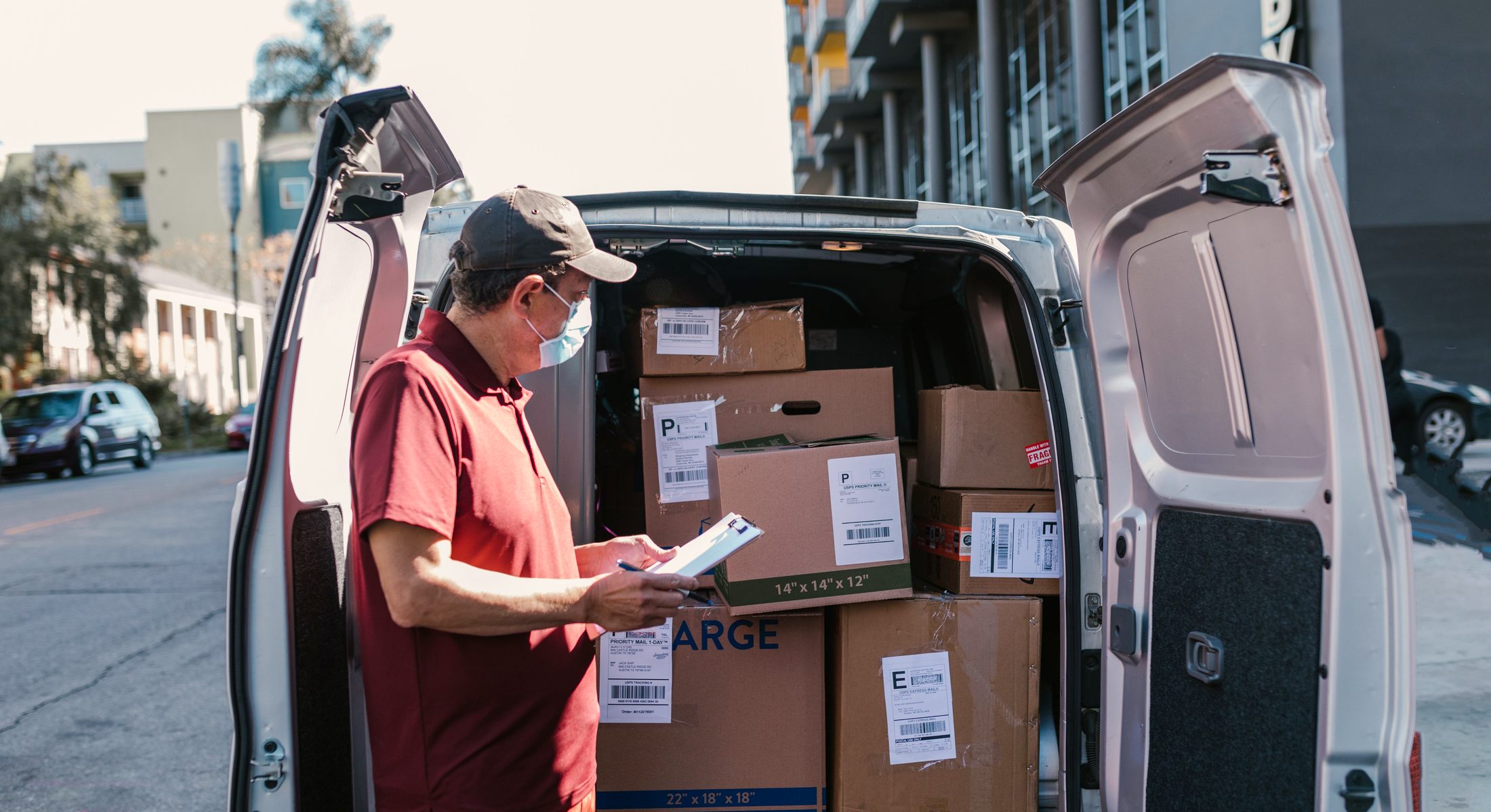A courier checking a delivery list at the open doors of a loaded van