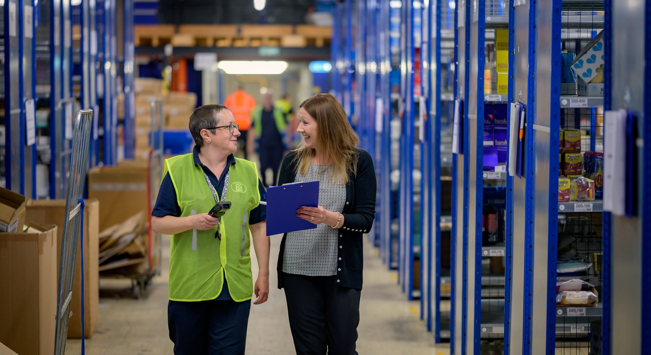 Two professionals walking a warehouse aisle, reviewing stock together