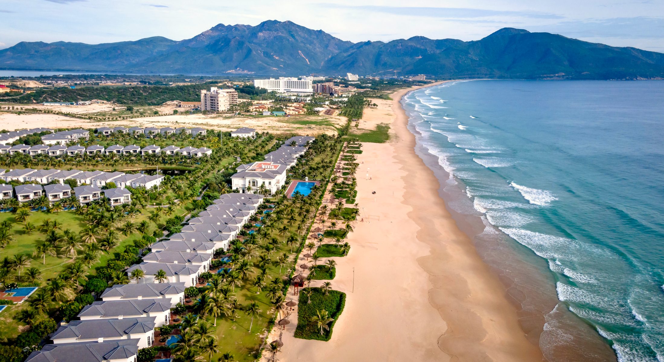 A coastal resort seen from the air, with mountains behind the bay