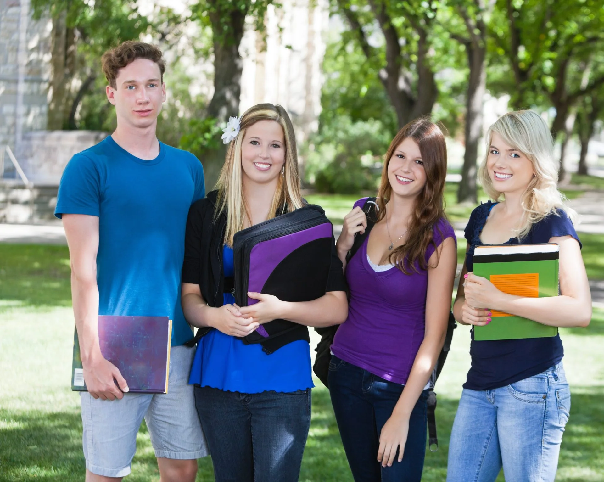 Four students standing together outdoors holding folders and notebooks