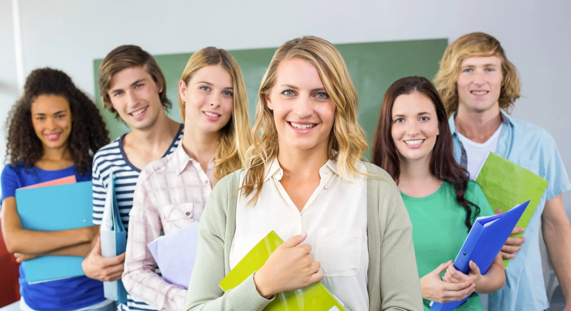 A group of learners holding folders and notebooks in a classroom
